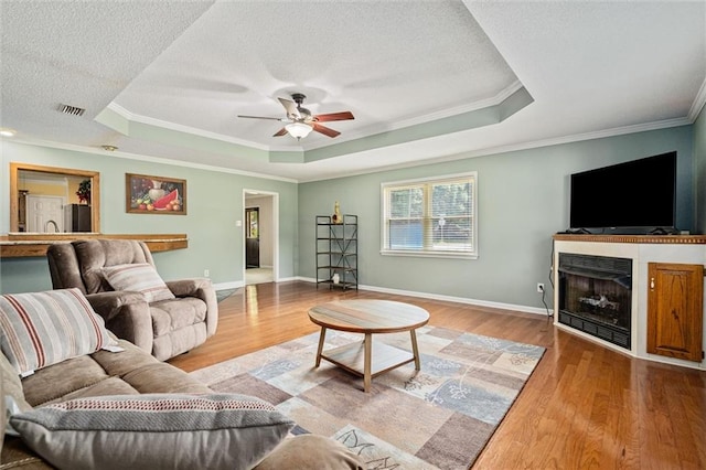 living room with light hardwood / wood-style flooring, a raised ceiling, and crown molding