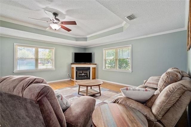 living room featuring crown molding, a textured ceiling, light wood-type flooring, ceiling fan, and a raised ceiling