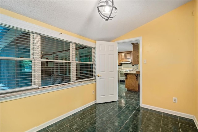 tiled empty room featuring vaulted ceiling and a textured ceiling