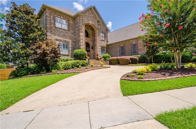 traditional-style home with driveway, a front yard, and brick siding