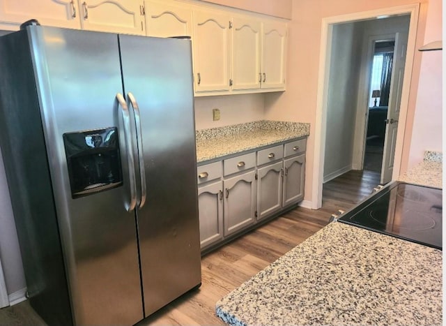 kitchen featuring white cabinetry, stainless steel fridge with ice dispenser, light hardwood / wood-style flooring, and light stone counters