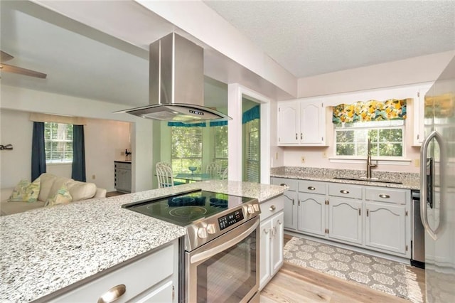 kitchen featuring wall chimney exhaust hood, light hardwood / wood-style floors, a healthy amount of sunlight, and appliances with stainless steel finishes