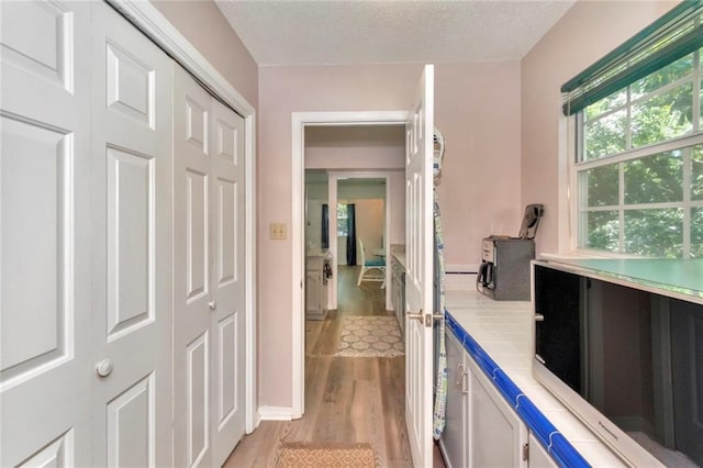 hallway with light wood-type flooring and a textured ceiling