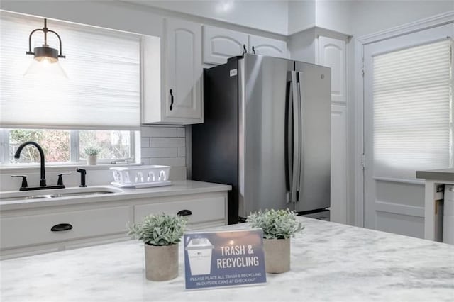 kitchen featuring decorative backsplash, stainless steel refrigerator, sink, pendant lighting, and white cabinetry