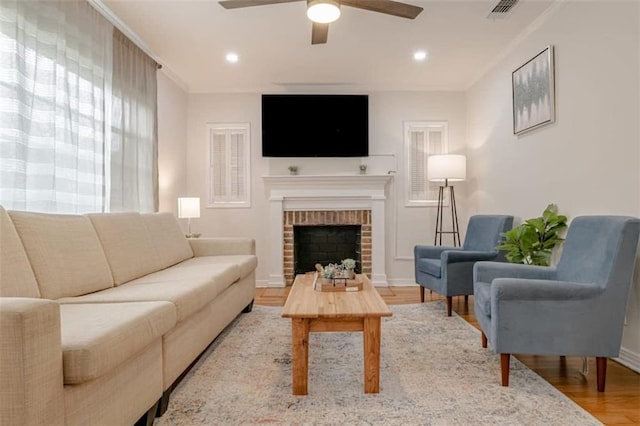 living room with ornamental molding, a brick fireplace, ceiling fan, and wood-type flooring