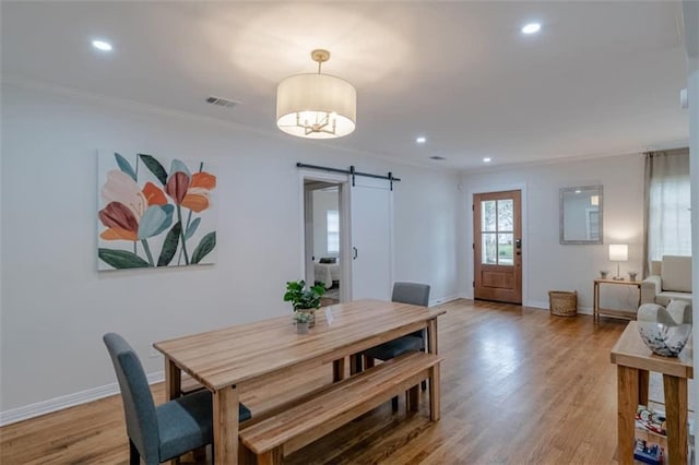 dining space with a barn door, wood-type flooring, and ornamental molding