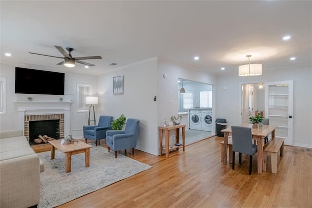 living room featuring ceiling fan, a brick fireplace, light hardwood / wood-style floors, and washer and clothes dryer