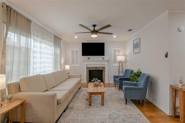 living room with ornamental molding, a fireplace, ceiling fan, and light hardwood / wood-style floors