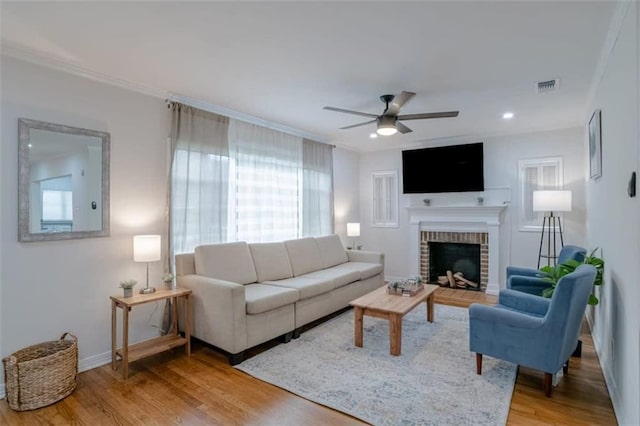 living room featuring wood-type flooring, a brick fireplace, ornamental molding, and ceiling fan