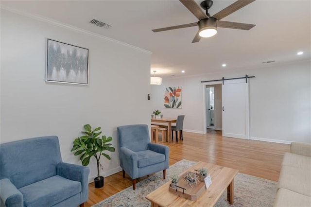 living room featuring a barn door, light hardwood / wood-style floors, crown molding, and ceiling fan