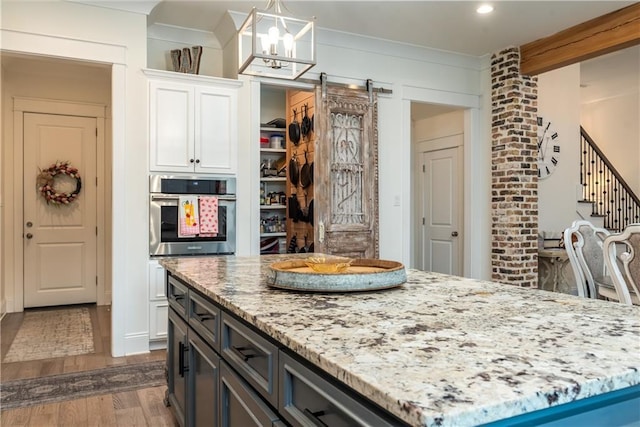 kitchen featuring light stone countertops, pendant lighting, stainless steel oven, white cabinets, and dark wood-style floors