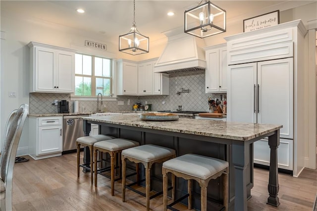 kitchen featuring white cabinets, a center island, stainless steel dishwasher, and custom exhaust hood