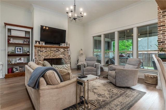 living area featuring crown molding, a brick fireplace, wood-type flooring, and a notable chandelier