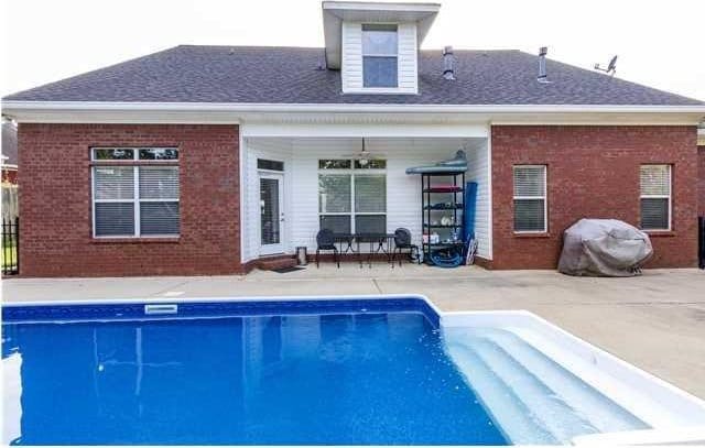 rear view of house featuring a patio area, an outdoor pool, and brick siding