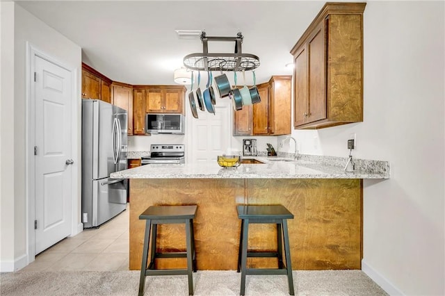 1933 Wildwood Pl, Mobile, AL 36609 - kitchen featuring brown cabinets, a sink, light stone counters, a peninsula, and stainless steel appliances