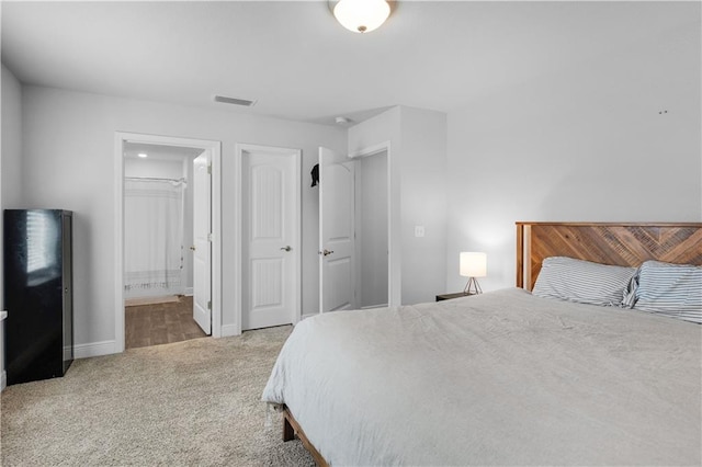 bedroom with carpet floors, visible vents, baseboards, and ensuite bathroom