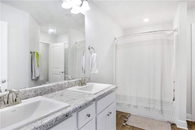 full bath with double vanity, wood finished floors, a sink, and visible vents