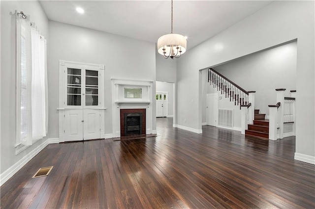 unfurnished living room featuring hardwood / wood-style flooring, a towering ceiling, and a notable chandelier