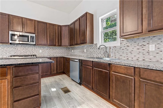 kitchen featuring tasteful backsplash, appliances with stainless steel finishes, light stone counters, sink, and dark brown cabinets