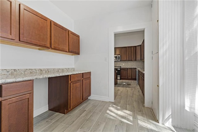 kitchen with light wood-type flooring, backsplash, range, and light stone countertops