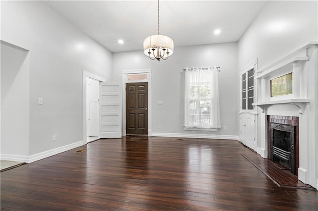 unfurnished living room with dark hardwood / wood-style floors, an inviting chandelier, and a brick fireplace