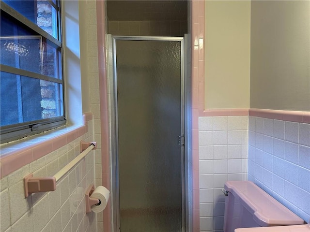 bathroom featuring toilet, a shower with shower door, and tile walls