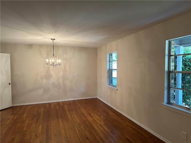 empty room with dark hardwood / wood-style floors and an inviting chandelier