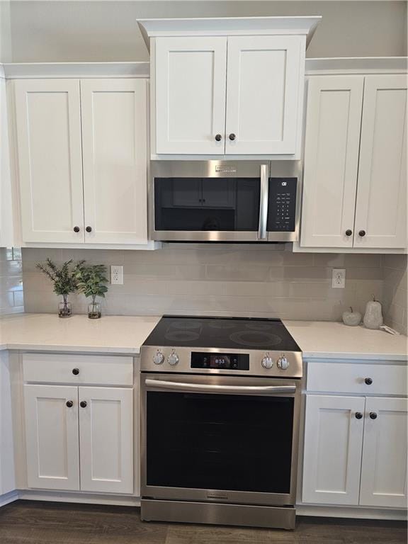 kitchen with appliances with stainless steel finishes, dark hardwood / wood-style floors, white cabinets, and decorative backsplash