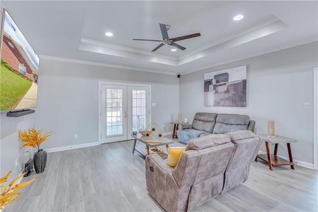 living room featuring french doors, a raised ceiling, ceiling fan, light hardwood / wood-style flooring, and crown molding