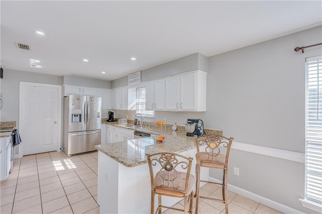 kitchen with light stone countertops, appliances with stainless steel finishes, white cabinetry, kitchen peninsula, and a breakfast bar area