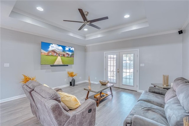 living room with ornamental molding, french doors, light wood-type flooring, and a raised ceiling