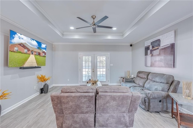 living room with a tray ceiling, ornamental molding, french doors, and light wood-type flooring