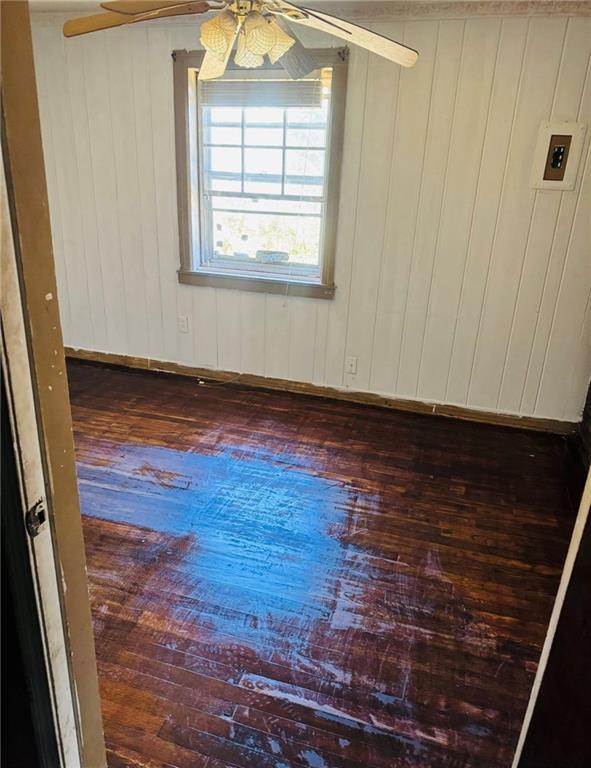 empty room with ceiling fan, dark hardwood / wood-style floors, and wood walls