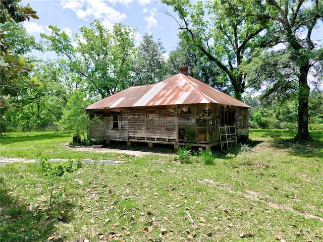 view of property exterior featuring metal roof, a chimney, and a lawn