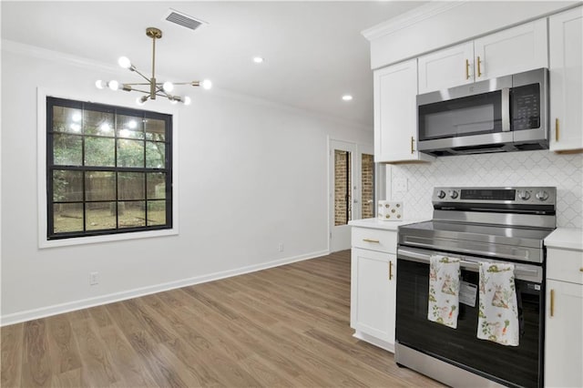 kitchen featuring stainless steel appliances, light countertops, white cabinets, and ornamental molding