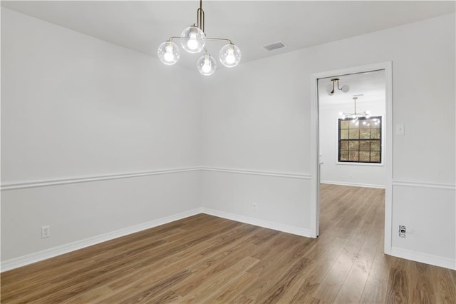 spare room with visible vents, a notable chandelier, baseboards, and wood finished floors