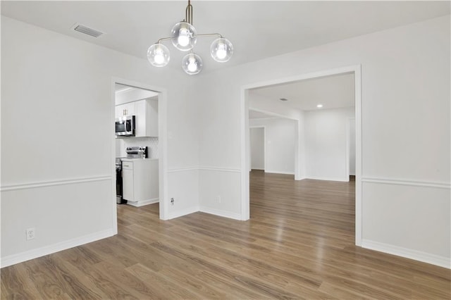 unfurnished dining area featuring an inviting chandelier, visible vents, baseboards, and wood finished floors