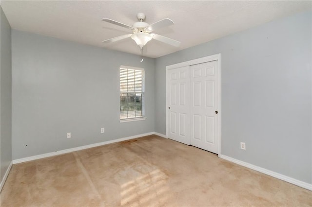 unfurnished bedroom featuring a ceiling fan, a closet, light colored carpet, and baseboards