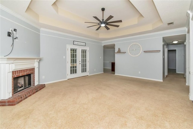 unfurnished living room with carpet floors, french doors, a raised ceiling, a brick fireplace, and ceiling fan