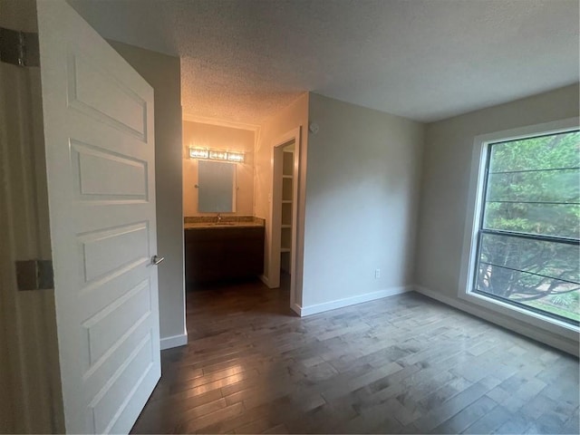 unfurnished bedroom with a textured ceiling, connected bathroom, hardwood / wood-style floors, and sink