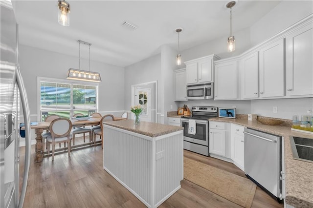 25504 Sunrise Ct, Loxley, AL 36551 - kitchen with stainless steel appliances, wood finished floors, a kitchen island, white cabinets, and decorative light fixtures