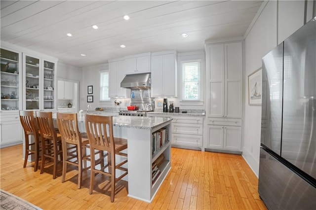 3009 Riverside Dr, Mobile, AL 36605 - kitchen featuring freestanding refrigerator, under cabinet range hood, light wood-style flooring, an island with sink, and white cabinetry