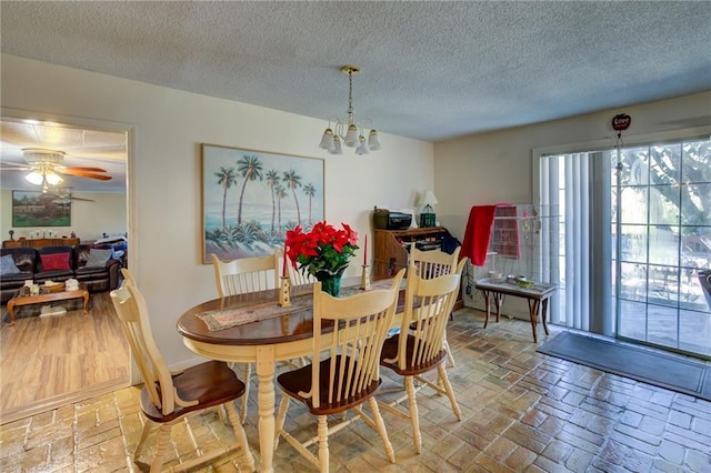 dining space featuring ceiling fan with notable chandelier and a textured ceiling