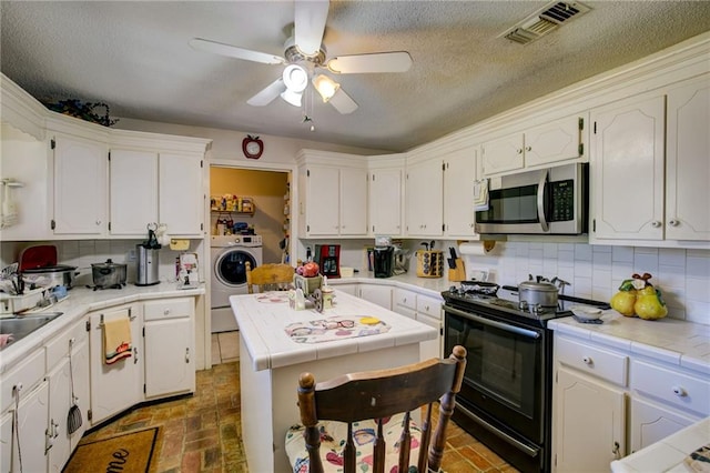 kitchen with white cabinets, tile counters, washer / clothes dryer, and black electric range