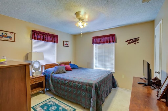 bedroom featuring ceiling fan, light carpet, and a textured ceiling