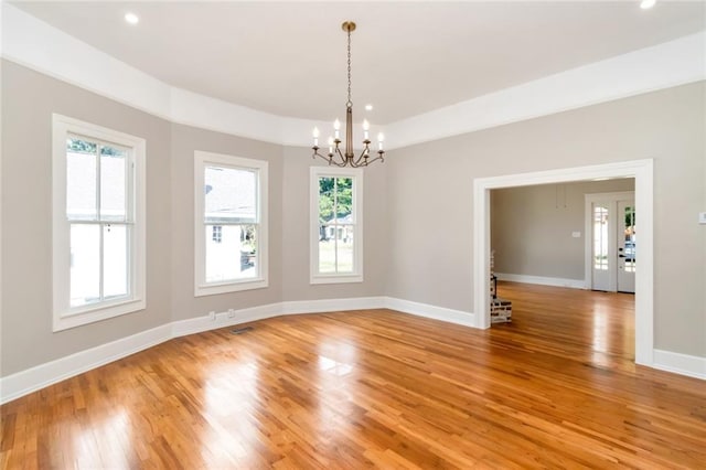 spare room with a wealth of natural light, a chandelier, and light wood-type flooring