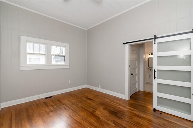 spare room featuring crown molding, hardwood / wood-style flooring, a barn door, and built in shelves