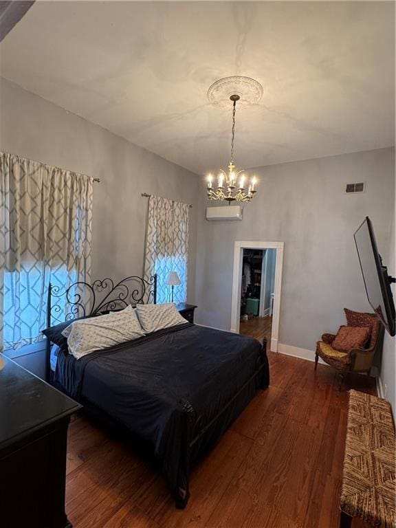 bedroom featuring an AC wall unit, dark wood-type flooring, and a notable chandelier