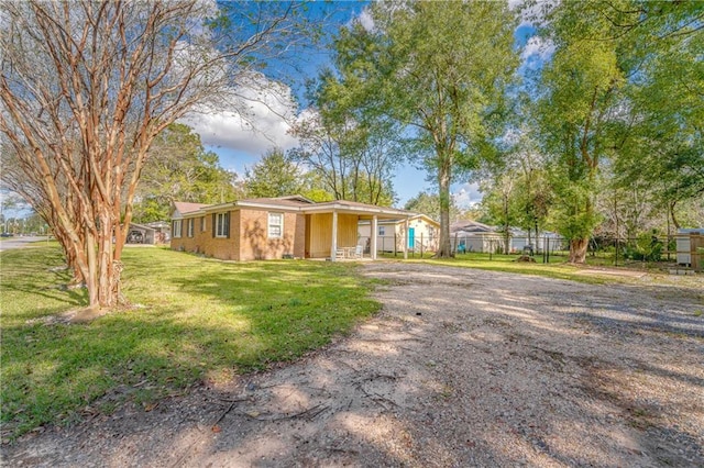 ranch-style home featuring brick siding, a front lawn, fence, a carport, and driveway