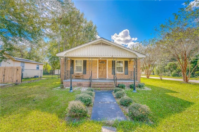 bungalow-style home featuring brick siding, a porch, a front yard, and fence